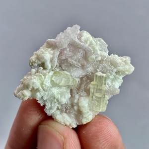 May include: A natural mineral specimen with pale green and pink tourmaline crystals set in a white matrix. The crystals are translucent, and the matrix has a rough texture. The overall shape is irregular. The specimen is a beautiful example of natural mineral formations.