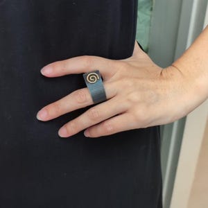 May include: A grey fabric ring with a gold spiral design.
