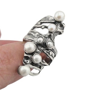 May include: A silver ring with a textured, organic design and multiple white pearls.