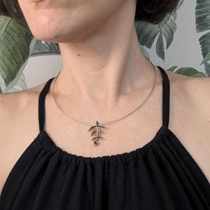 May include: A silver necklace with a delicate branch pendant featuring a small red gemstone. The necklace is worn by a person with a black top.