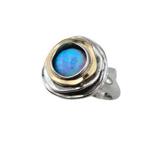 Pode incluir: Um anel de prata com uma pedra de opala azul engastada em uma moldura de ouro. O anel tem um design texturizado e orgânico.