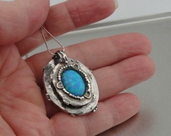 May include: A silver pendant with a blue opal gemstone set in a textured, hammered silver frame. The pendant is on a silver chain.