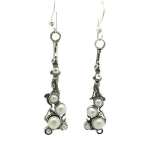 Puede incluir: Un par de pendientes de plata con un racimo de perlas blancas en cada pendiente. Los pendientes tienen un diseño delicado y orgánico.