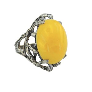 May include: A silver ring with a large, oval, yellow gemstone. The ring has an elaborate, openwork design. The gemstone is a vibrant yellow, set within a detailed, textured silver setting.