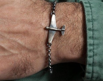 May include: A silver bracelet with a small airplane charm. The bracelet is made of a chain link design.