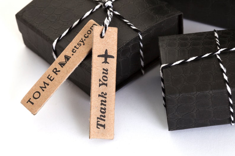 K&ouml;nnte beinhalten: Zwei kleine schwarze Geschenkboxen mit einem wei&szlig;en und schwarzen Band darum gebunden. Eine Box hat ein braunes Etikett mit der Aufschrift "TOMERM.etsy.com" und die andere ein braunes Etikett mit der Aufschrift "Danke" und einem kleinen Flugzeugsymbol.