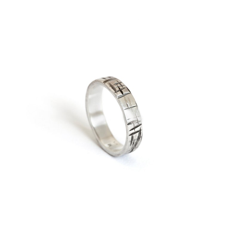 K&ouml;nnte beinhalten: Ein silberner Bandring mit einem strukturierten Design. Der Ring ist aus Metall und hat eine polierte Oberfl&auml;che.