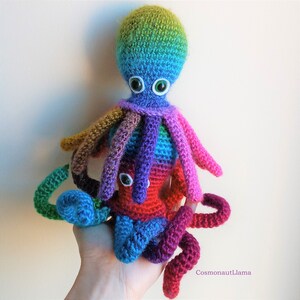 May include: A colorful crocheted octopus with large green eyes. The octopus is made with a variety of colors, including red, blue, green, purple, and yellow.