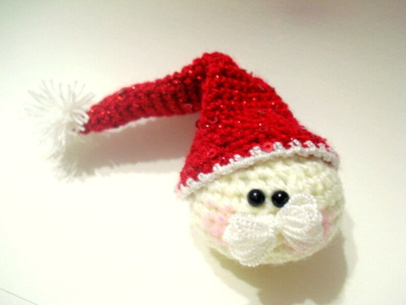 Op de afbeelding: Een gehaakte sneeuwman ornament met een rode kerstmanmuts en witte rand. De sneeuwman heeft zwarte ogen, een witte snor en roze wangen.