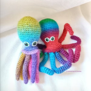 May include: Two crocheted octopus plushies with rainbow colored yarn. The octopus on the left has brown, purple, and pink tentacles. The octopus on the right has blue, green, and red tentacles.