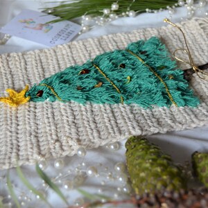 May include: A green and gold Christmas tree wall hanging with a white background. The tree is made of yarn and has a gold star on top. The tree is decorated with gold string and small red and gold beads.
