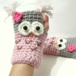 May include: A pair of pink and gray crocheted owl fingerless gloves with black eyes and pink flower accents.