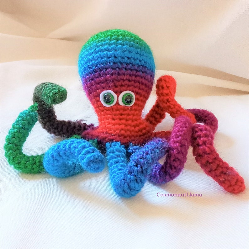 May include: A crocheted octopus with rainbow colored tentacles and green eyes. The octopus is made with a variety of colors, including red, orange, yellow, green, blue, and purple.