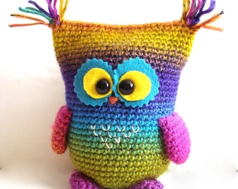 May include: A colorful crocheted owl toy with rainbow yarn and large yellow eyes. The owl has a blue felt beak and a white stitched heart on its chest.