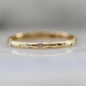 Puede incluir: Un anillo dorado con un pequeño diamante en el centro. El anillo está adornado con grabados en forma de estrella alrededor de la banda. Una delicada joya.