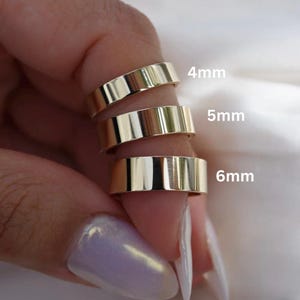 Puede incluir: Se muestran tres anillos dorados con un diseño de banda plana. Los anillos están etiquetados con los tamaños: 4 mm, 5 mm y 6 mm. Los anillos se muestran en un dedo, con los tamaños claramente visibles.