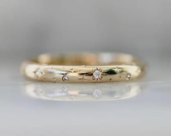 Op de afbeelding: Een goudkleurige ring met een afgeronde band. De ring is versierd met kleine, sprankelende edelstenen en stervormige gravures. De edelstenen zijn vlak ingezet en de ring heeft een gepolijste afwerking.