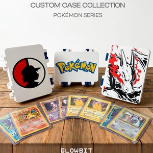 May include: Three white rectangular storage cases with blue latches, featuring graphics of a silhouette, the Pokémon logo, and a Charizard illustration. Below are several trading cards in clear protective sleeves, including Charizard and Lugia.