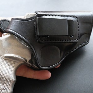 May include: A black leather holster with a metal clip for a small silver handgun.