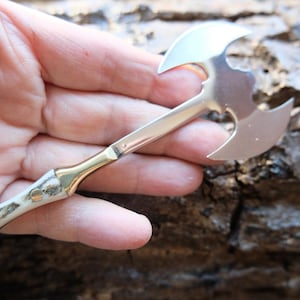 May include: A small, silver double-headed axe keychain with a bone-like handle and a gold-colored accent.