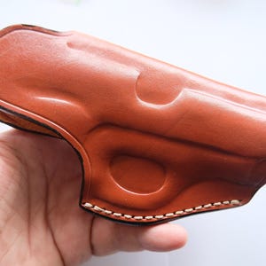 Op de afbeelding: Een bruine leren holster met een gestikte rand.