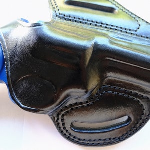 Pode incluir: 冷たさ、黒革ホルスター、青色の銃が中に入っている。ホルスターはステッチとベルトループが付いている。