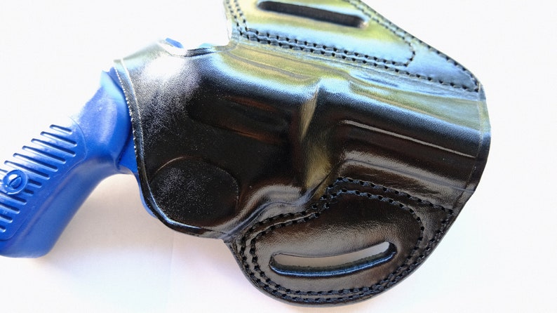 Pode incluir: 冷たさ、黒革ホルスター、青色の銃が中に入っている。ホルスターはステッチとベルトループが付いている。