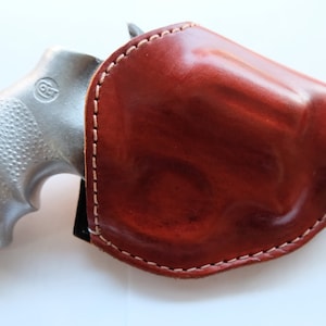 May include: A silver revolver with a brown leather holster. The holster has white stitching around the edges.