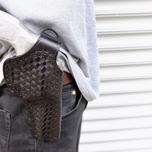 May include: A person wearing a grey sweater and black jeans with a brown leather holster and a silver handgun tucked into the waistband.