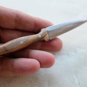 Puede incluir: Un pequeño cuchillo con mango de madera y hoja de plata. El mango tiene tres detalles plateados.