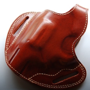 Op de afbeelding: Een bruine leren holster met witte stiksels. De holster heeft een klep die de opening bedekt.