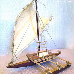 May include: A handcrafted wooden model of a Polynesian outrigger sailing canoe. The model features a dark brown hull, a light-colored sail, and intricate detailing with natural materials. The text "THE LASHED LUG" is visible on the upper right.