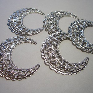 May include: Four silver-toned metal filigree charms shaped like crescent moons. Each charm features an intricate, openwork lattice pattern with a scalloped outer edge, reflecting light across the metallic surface of the crescent moon shapes.