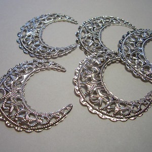 May include: Four silver-toned metal crescent moon charms featuring an intricate filigree cutout pattern. Each piece has a scalloped edge and a reflective metallic finish, arranged in a cluster to display the detailed openwork design.
