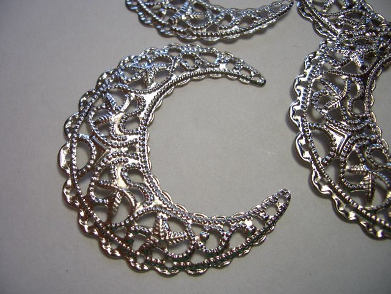 May include: Three silver-toned metal filigree components shaped like crescent moons. Each piece features an intricate, openwork pattern with small, raised beaded textures along the edges and throughout the delicate, swirling design.