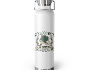 Könnte beinhalten: Eine weiße zylindrische Wasserflasche mit einem silbernen Metalldeckel und Griff. Auf der Vorderseite befindet sich eine Grafik eines grünen Pickleball-Schlägers und Balls mit dem Text IT'S A GOOD DAY TO PLAY PICKLEBALL THE COURT CLUB EST. 2026 in Dunkelgrün und Beige.