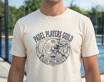 Könnte beinhalten: Ein cremefarbenes T-Shirt mit einem marineblauen Grafikdesign. Das Design enthält den Text "PADEL PLAYERS GUILD" und "GLASS WALL SOCIETY" mit einer Illustration eines Padelspielers. Das Shirt besteht aus einem weichen, strukturierten Material.