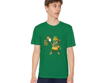 Könnte beinhalten: Grünes T-Shirt mit einem Cartoon-Gurken-Pickleball-Spieler. Die Gurkenfigur trägt ein gelbes Hemd, ein orangefarbenes Stirnband und orangefarbene Schuhe. Der Text auf dem Shirt lautet "Just Dill With It."
