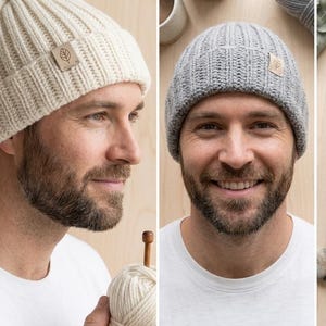 May include: A cream-colored ribbed knit beanie with a pom-pom and a light brown square tag featuring a leaf icon, alongside a grey ribbed knit beanie with a matching light brown square tag featuring a leaf icon, both made of yarn.
