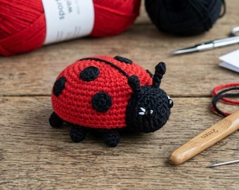 May include: A crocheted ladybug toy with a bright red body featuring black circular spots and a solid black head. The ladybug has two small antennae and black bead eyes with white accents. It is crafted from yarn and sits on a wooden surface.