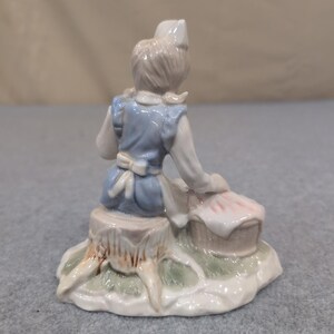Statuetta vintage in porcellana raffigurante un'infermiera con un cucciolo in un cestino, nei colori blu e bianco. immagine 4