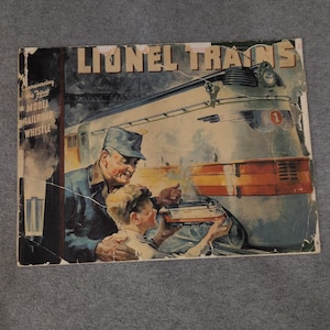 Könnte beinhalten: Vintage Lionel Trains-Werbung mit einem silber-blauen Zug. Ein Mann und ein Junge betrachten ein Modell des Zuges. Der Titel lautet "Lionel Trains" und "Announcing the First Model Railroad Whistle".