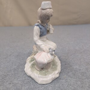 Statuetta vintage in porcellana raffigurante un'infermiera con un cucciolo in un cestino, nei colori blu e bianco. immagine 5