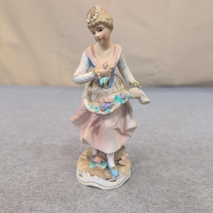 Estatueta vintage de porcelana biscuit representando uma mulher com uma cesta de flores em tons de rosa, azul e branco. imagem 1