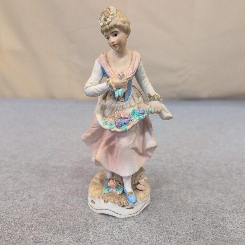Estatueta vintage de porcelana biscuit representando uma mulher com uma cesta de flores em tons de rosa, azul e branco. imagem 1