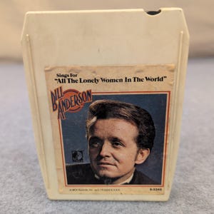 Könnte beinhalten: Vintage 8-Spur-Kassette mit Bill Anderson. Das Etikett zeigt "Sings For 'All The Lonely Women In The World'" und ein Porträt von Anderson. Die Kassette befindet sich in einer cremefarbenen Kunststoffkartusche.