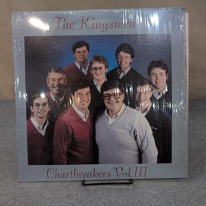 May include: A vinyl record album titled "The Kingsmen Chartbreakers Vol. III" featuring a group of men in sweaters and collared shirts. The album cover is encased in clear plastic.