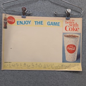 Könnte beinhalten: Vintage Coca-Cola-Werbung mit den Slogans "Enjoy the Game" und "Things go better with Coke." Das Poster zeigt eine Coca-Cola-Flasche und einen Becher Coke. Schiedsrichterzeichen unten.