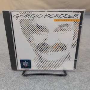 May include: A Giorgio Moroder CD in a clear plastic case. The album cover features a stylized portrait and the text "Giorgio Moroder" and "16 Early Hits". A "Special Price" sticker is on the lower left corner.