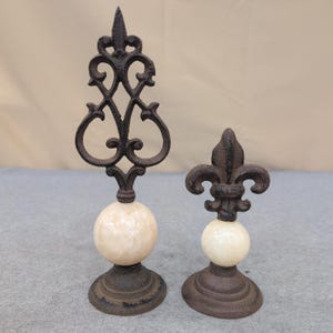 Juego de 2 remates decorativos de hierro fundido y piedra con diseño de flor de lis, color marrón crema. imagen 1